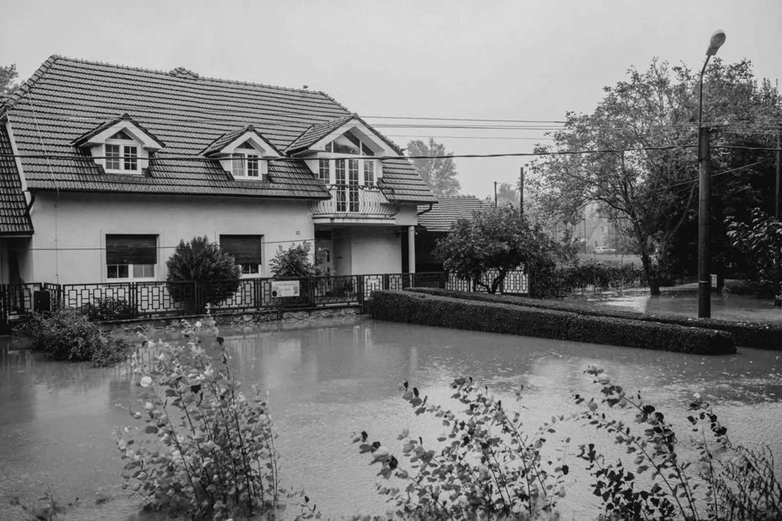 Une rue inondée après une crue, maison et voiture partiellement submergées sous un ciel couvert